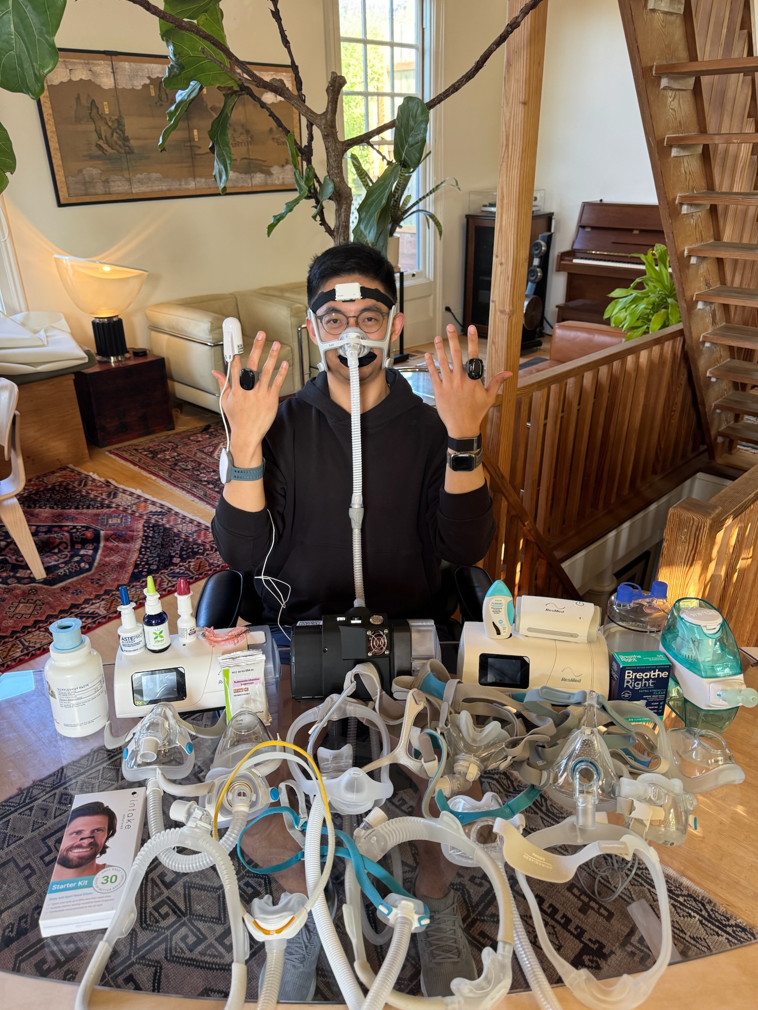 Rhythm Co-Founder Reginald Long wearing a PAP mask, seated behind a table of sleep apnea treatments and devices